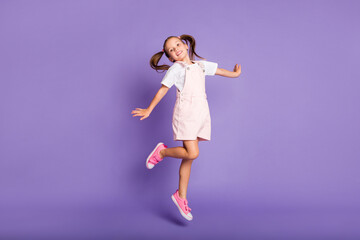 full body photo of dreamy positive little girl jump up air wear pink shoes isolated on purple color 