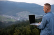 Man working outdoors with laptop in mountains. Concept of remote work or freelancer lifestyle. Cellular network broadband coverage. internet 5G.