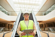 Graphic Waist Up Portrait Of Mixed-race Female Worker Looking At Camera And Holding Clipboard While Standing Against Escalator In Business Mall, Copy Space