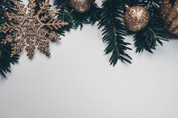 Christmas background with spruce branches and golden glitter baubles and snowflake or stars decorations all laid on white background. Copy space with decorations on top.