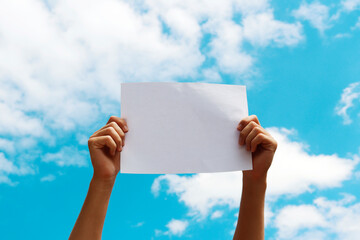 a blank sheet of paper in the hands of a young guy against a blue sky with clouds