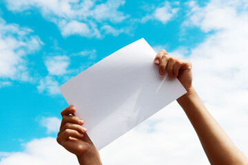 a blank sheet of paper in the hands of a young guy against a blue sky with clouds