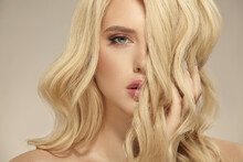 Female Beauty, Hairstyle Of Blonde Long Wavy Hair. Caucasian Attractive Woman Has A Natural Curly Hairstyle, Close Up Shot On A Beige Isolated.