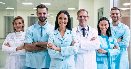 Happy team of successful and confident modern medical doctors are posing and looking on the camera at the hospital corridor