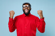 © ViDi Studio - Happy joyful young bearded african american man 20s wearing casual red shirt cap eyeglasses standing doing winner gesture clenching fists isolated on pastel blue color background studio portrait.