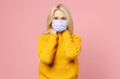 © ViDi Studio - Elderly gray-haired blonde woman lady 40s 50s in yellow sweater sterile face mask safe from coronavirus virus covid-19 during quarantine put hands on neck isolated on pink background studio portrait.