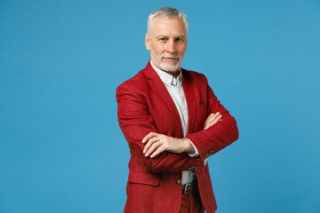 Smiling successful confident elderly gray-haired mustache bearded business man wearing red jacket suit standing holding hands crossed looking camera isolated on blue color background studio portrait.