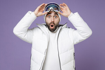 Wall Mural - Shocked skier man in warm white windbreaker jacket ski goggles mask keeping mouth open going to spend weekend winter season in mountains isolated on purple background. People lifestyle hobby concept.