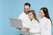 © ViDi Studio - Smiling young parents mom dad with child kid daughter teen girl in white sweaters working on laptop pc computer isolated on blue background studio portrait. Family day parenthood childhood concept.