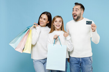 Wall Mural - Excited young parents mom dad with child kid daughter teen girl hold package bags purchases after shopping credit bank card showing thumb up isolated on blue background. Family day parenthood concept.