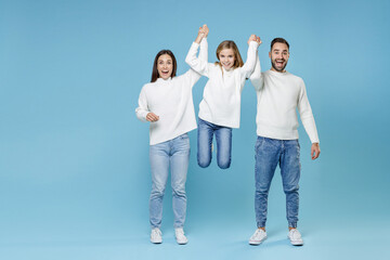 Wall Mural - Full length of excited funny young happy parents mom dad holding child kid daughter teen girl in white sweaters jumping isolated on blue background studio portrait. Family day parenthood concept.