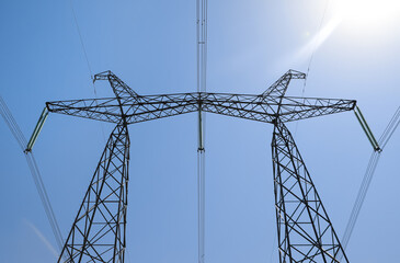 High voltage tower with electricity transmission power lines against blue sky, low angle view