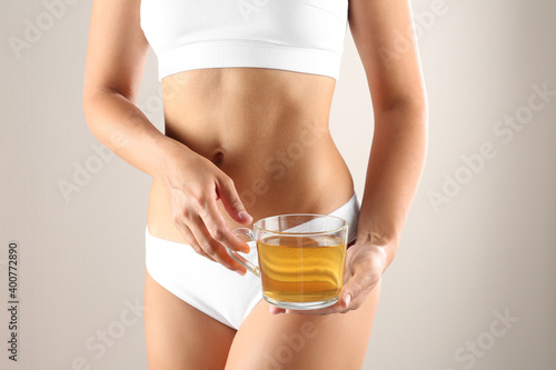 Young woman holding cup of diet tea on beige background, closeup