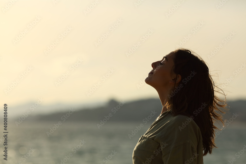 Back light of woman silhouette breathing fresh air on the beach - obrazy, fototapety, plakaty 