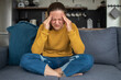 © molenira - Woman with headache holding head on couch in kitchen or living room