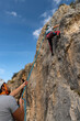 Girl in the middle of a rock wall that is climbing while her boyfriend belays her from below
