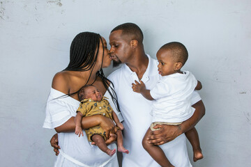 A beautiful African-American young family with two children. The oldest son is a toddler and the new infant newborn son is only a few weeks old. Mom and Dad are kissing