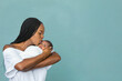 © Ursula Page - A beautiful young African-American woman with braids is kissing her newborn son and looking at him with love on a teal blue background.