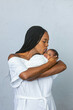 © Ursula Page - A beautiful young African-American woman with braids is kissing her newborn son and looking at him with love on a white gray background and giving him a kiss