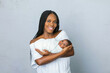 © Ursula Page - A beautiful young African-American woman with braids is holding her newborn son and looking at the camera with a white gray background with copy space