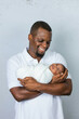 © Ursula Page - An attractive African-American new father is holding his newborn son and looking at him  with affection on a white-gray background.