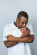 © Ursula Page - An attractive African-American new father is holding his newborn son and giving him a kiss with a white-gray background.