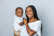 © Ursula Page - A beautiful young African-American woman with braids is holding her toddler age cute son and looking at the camera with a white gray background.