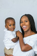 © Ursula Page - A beautiful young African-American woman with braids is holding her toddler age cute son and looking at the camera with a white gray background.