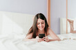 © Eva Blanco/Westend61 - Smiling beautiful woman text messaging while lying on bed at home