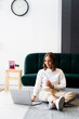 © Westend61 - Businesswoman with coffee cup using laptop while sitting on floor at office
