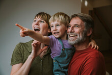 Smiling Father Carrying Son Pointing While Mother Looking Away Standing At Home
