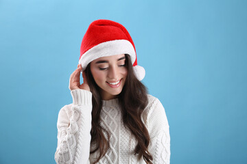 Wall Mural - Beautiful woman wearing Santa Claus hat on light blue background