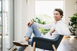 © UWE_UMSTAETTER/Westend61 - Smiling mid adult man sitting on chair at home