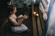 © irissca - Young woman sitting on the floor, lights candles, enjoy meditation, do yoga exercise at home. Mental health, self care, No stress, healthy habit, mindfulness lifestyle, anxiety relief concept
