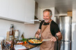 © VALENTINA BARRETO STUDIO/Westend61 - Smiling mature man preparing pasta while standing in kitchen at home