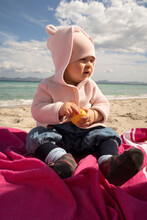 Baby Girl Sitting On Sand At Beach During Sunny Day