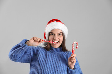 Sticker - Pretty woman in Santa hat and blue sweater eating candy cane on grey background