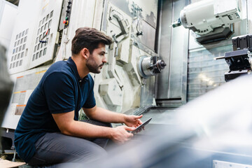Male worker analyzing machines while holding digital tablet in factory