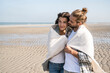 © UWE_UMSTAETTER/Westend61 - Romantic young couple covered in blanket standing at beach