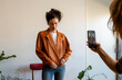 © VALENTINA BARRETO STUDIO/Westend61 - Female friend taking photo of beautiful woman on smart phone standing at home