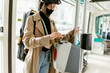 © VALENTINA BARRETO STUDIO/Westend61 - Woman wearing face mask and cycling helmet putting ticket in ticket validation machine while standing in tram