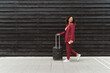 © Mikel Taboada/Westend61 - Young businesswoman looking back while walking with luggage on footpath by black wooden wall in city