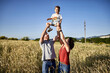 © victor espadas gonzalez/Westend61 - Playful parents picking up son while standing amidst crops against clear blue sky
