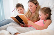 © Jamie Grill/Tetra Images - Mother reading with daughter (6-7) and son (8-9)