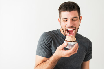 Handsome latin guy is about to take a bite of a cupcake