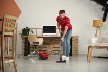 Wall Mural - Young man using vacuum cleaner at home