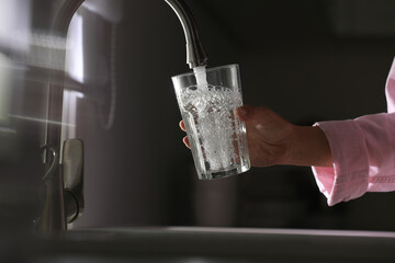 Canvas Print - Woman pouring water into glass in kitchen, closeup