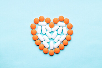 Wall Mural - heart symbol formed orange pills or tablets isolated on a blue background. above view. outer space. cardiac medicine concept