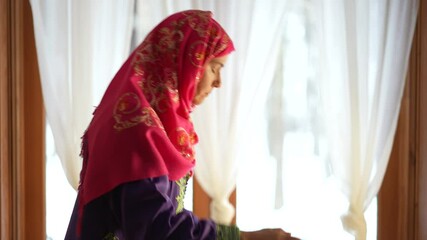 Wall Mural - Mature Muslim woman praying at home with beautiful light with snow on the ground. Concept of female prayer in home environment.