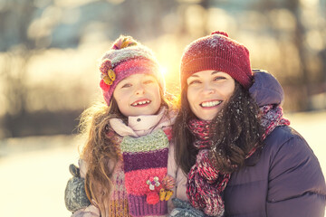 Little girl and her mother playing outdoors at sunny winter day. Active winter holydays concept.